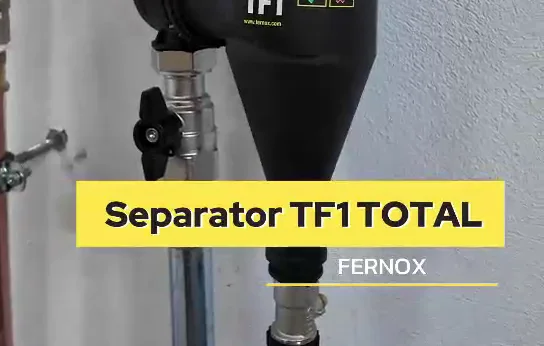 Czarny separator zanieczyszczeń z armaturą, zamontowany pionowo przy ścianie